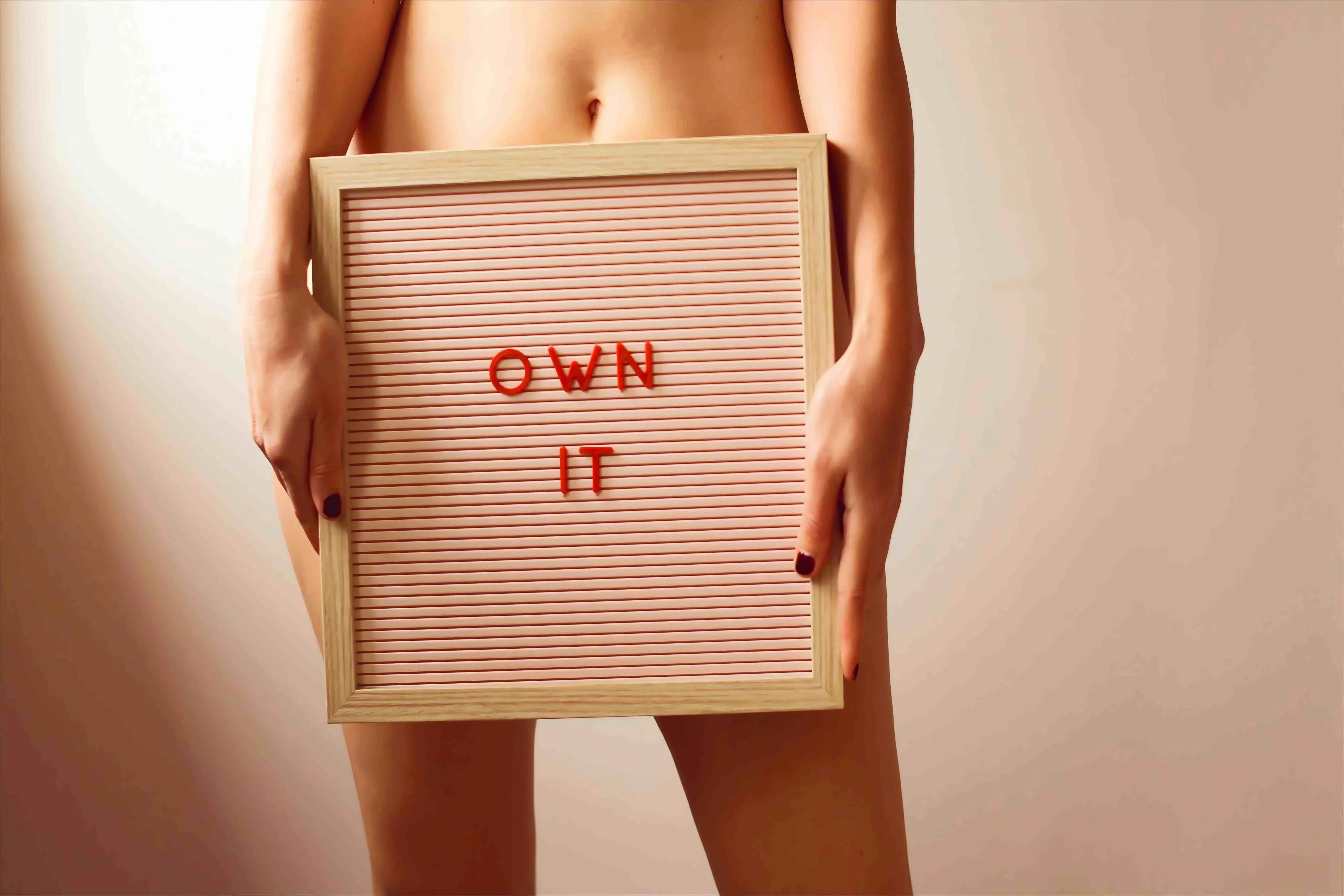 SHEVEREIGN blog banner image of a woman holding a sign reading “OWN IT,” symbolizing confidence, body autonomy, and empowerment in women’s sexual health awareness