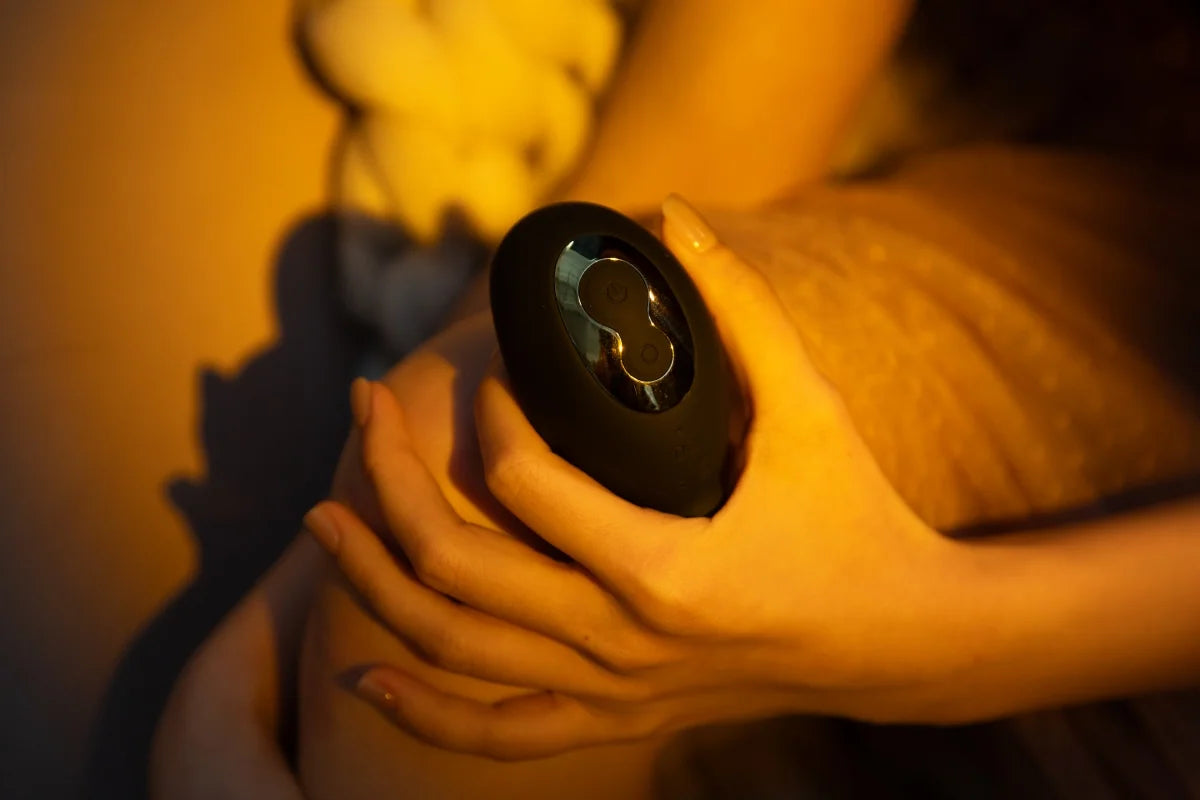 SHEVEREIGN Obsidian Tease clit vibrator product detail image showing its dual suction and licking design in a warm intimate setting with soft black gold finish and refined sensual elegance