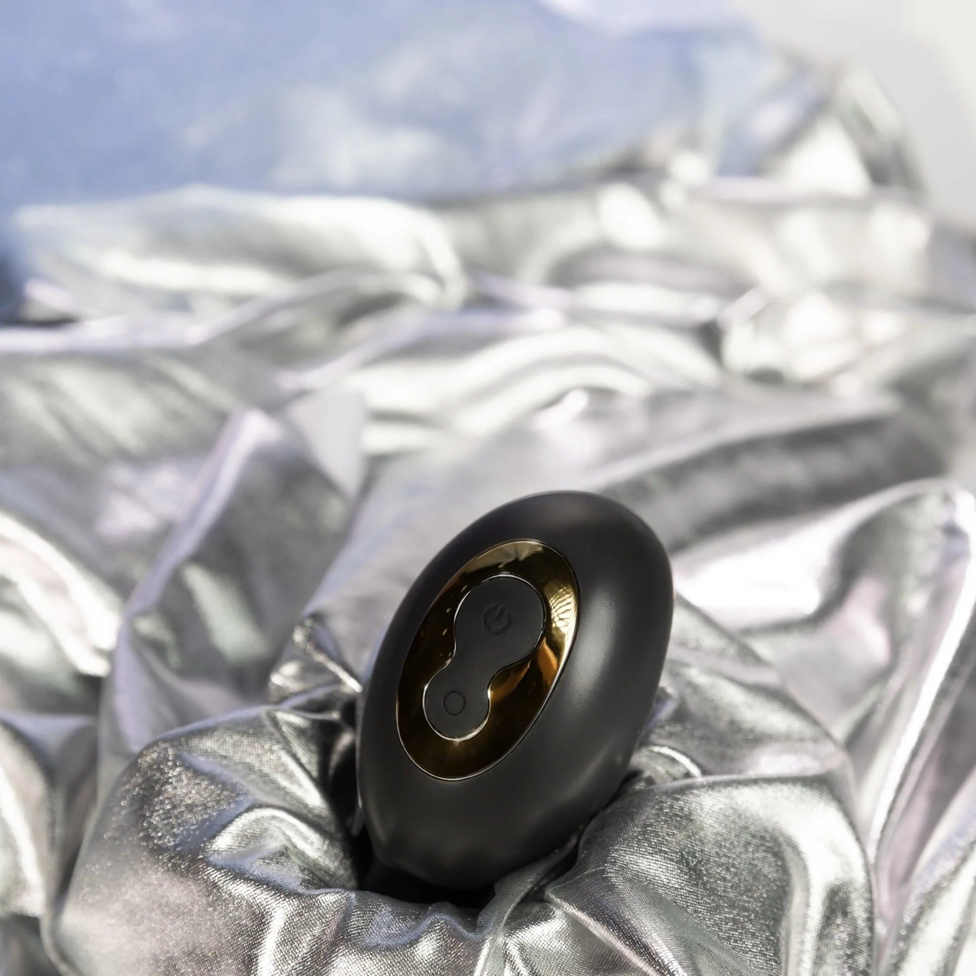 SHEVEREIGN Obsidian Tease clit vibrator displayed on soft satin fabric, showing its black gold design and dual zone stimulation in an elegant intimate setting