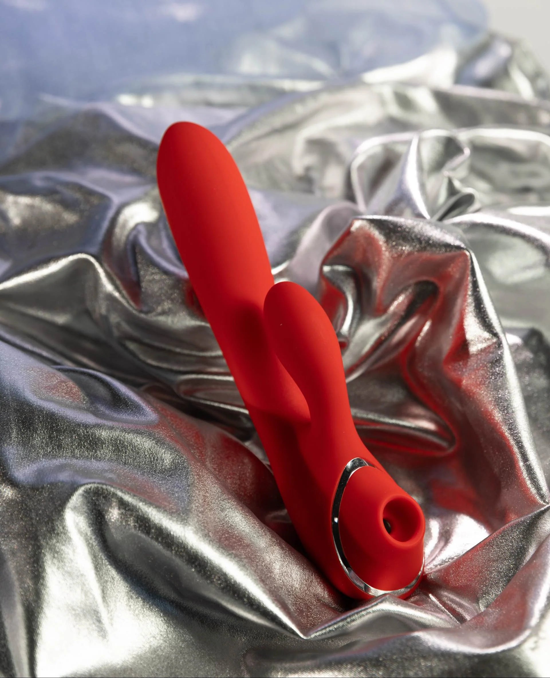 SHEVEREIGN Scarlet Kiss clit vibrator displayed on silver satin, highlighting its red dual-zone suction and vibration design with an elegant sculpted form