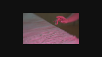SHEVEREIGN lifestyle video thumbnail featuring a woman’s hand gliding softly over textured fabric under warm pink lighting, reflecting a calm feminine atmosphere